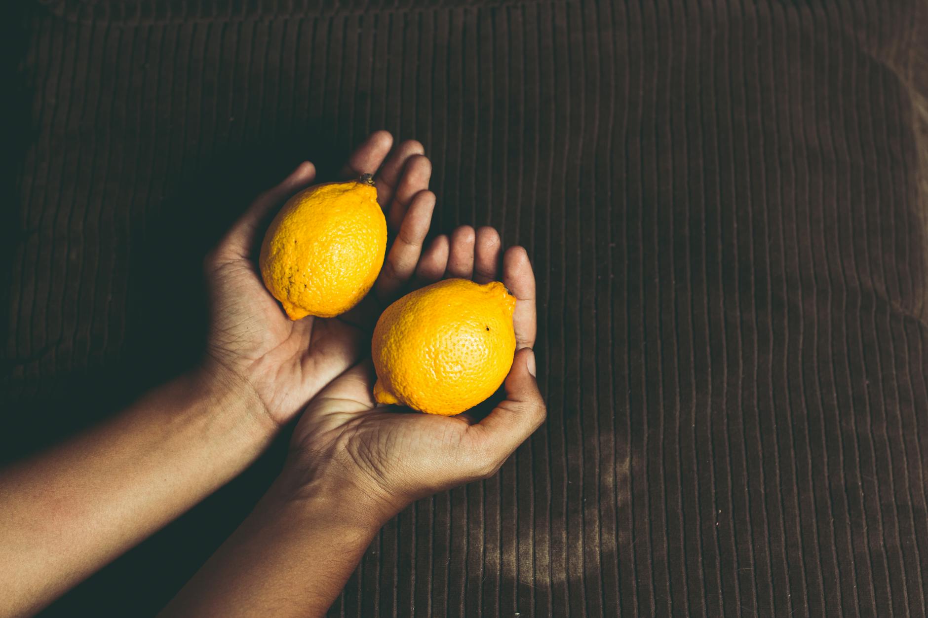 Hand holding a fresh yellow lemon against vibrant yellow background, symbolizing renewed pleasure and vitality