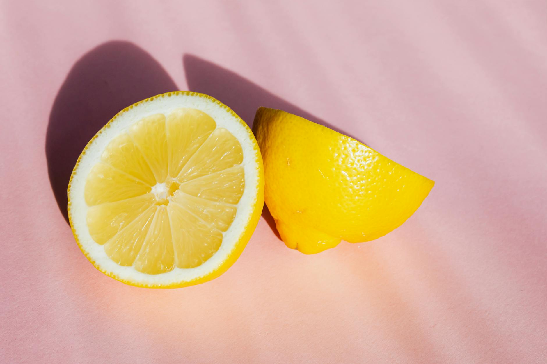 Una composizione con limoni gialli freschi sbucciati su uno sfondo rosa al sole.