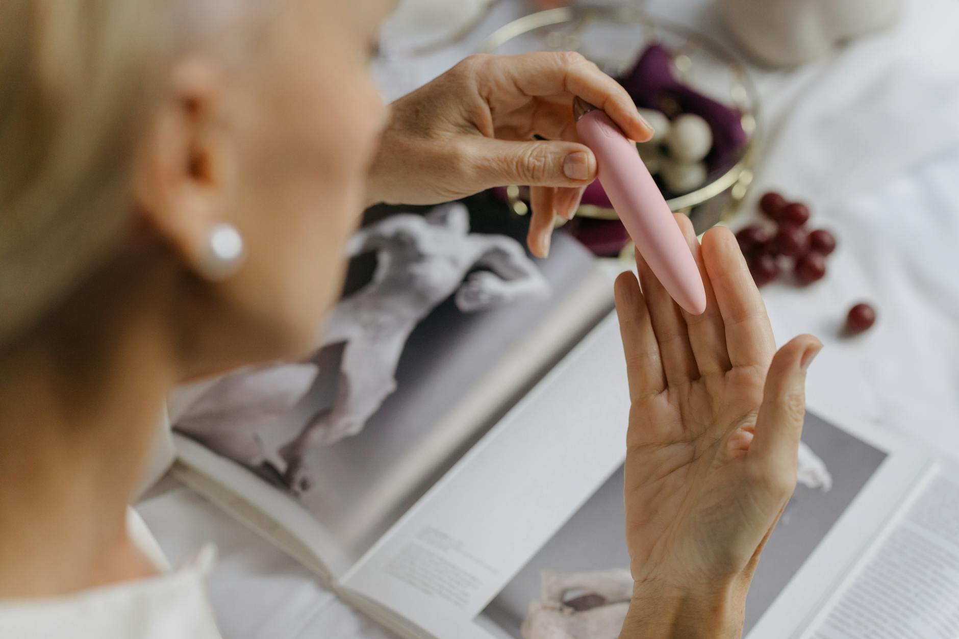 Donna che tiene in mano un vibratore rosa brillante, con libri d'arte sullo sfondo, sottolineando temi intimi e personali