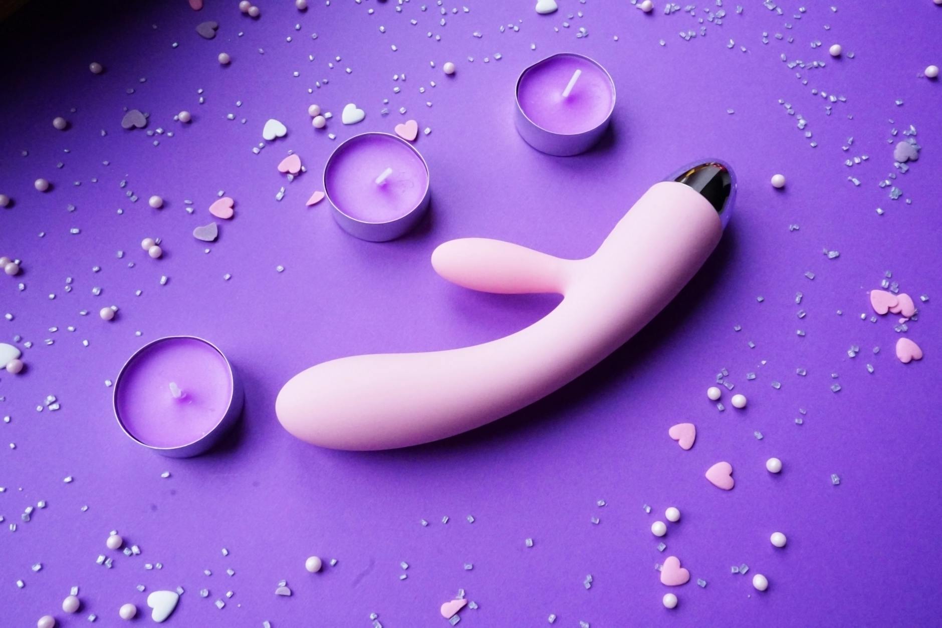 A pink vibrator on a purple background with heart confetti and candles for a romantic vibe